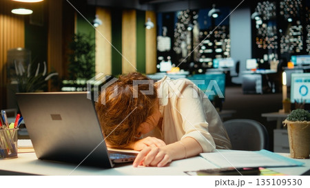 General manager in a dark office at midnight struggles to stay awake after an intense workload, dealing with anxiety due to work tension and fatigue. Mental haze and workplace challenges. Camera A. 135109530