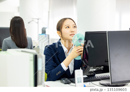 扇風機をオフィスで使う若い女性 扇風機をオフィスで使う若い女性 135109603