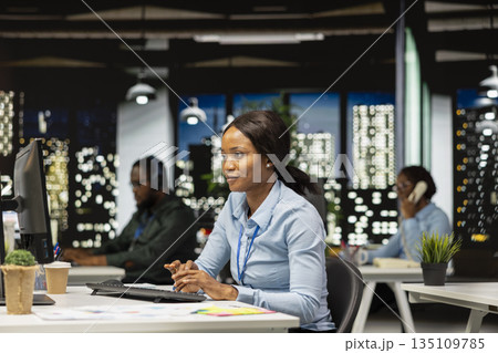 Black female works on researching and documenting reports after hours, data updates and business enterprise, after hours work in a dark office. Finance targets and project development. 135109785