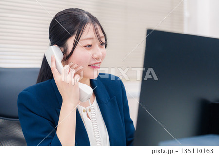 オフィスの固定電話で通話をする女性ビジネスパーソン オフィスの固定電話で通話をする女性ビジネスパーソン 135110163