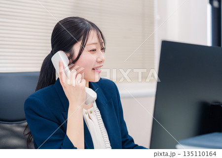 オフィスの固定電話で通話をする女性ビジネスパーソン オフィスの固定電話で通話をする女性ビジネスパーソン 135110164