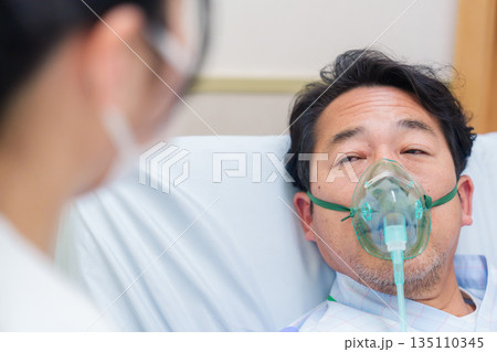 人工呼吸器をつけて話をする入院患者の男性 人工呼吸器をつけて話をする入院患者の男性 135110345