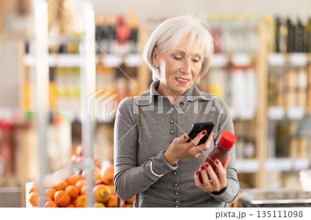 Elderly woman scanning qr code for ketchup Elderly woman scanning qr code for ketchup 135111098