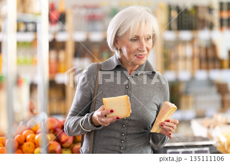 Elderly woman choosing cheese in grocery store Elderly woman choosing cheese in grocery store 135111106