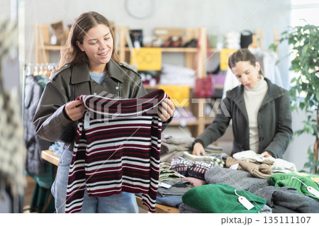 Happy girl chooses fashionable sweater for autumn winter season in store 135111107