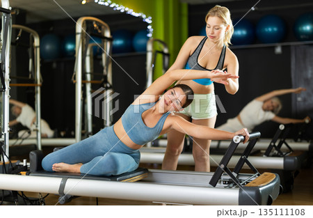 qualified trainer assists the client in a Pilates class 135111108