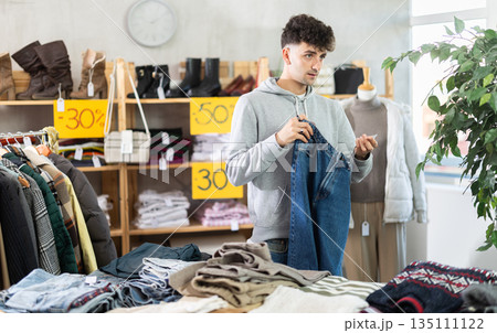 Young guy choosing jeans during fall sale Young guy choosing jeans during fall sale 135111122