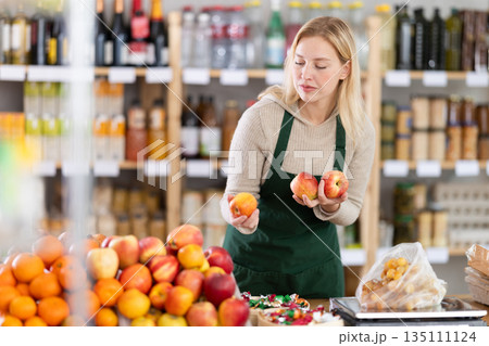Young woman seller weighs apples in grocery store 135111124
