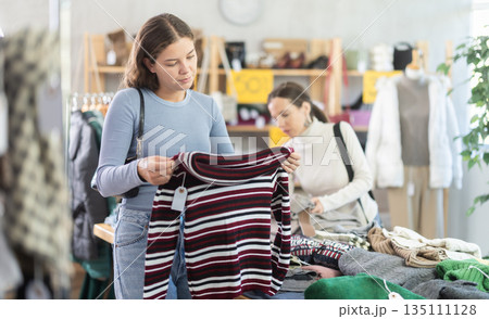 Attentive young girl choosing sweater in clothing store Attentive young girl choosing sweater in clothing store 135111128