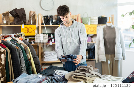 Young guy choosing jeans pantaloons in clothing store Young guy choosing jeans pantaloons in clothing store 135111129