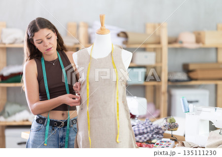 Dressmaker constructing custom dress on mannequin in sewing workshop 135111230