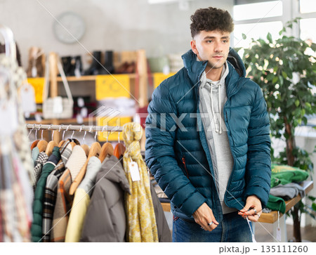 Young man trying on down jacket in clothing store 135111260