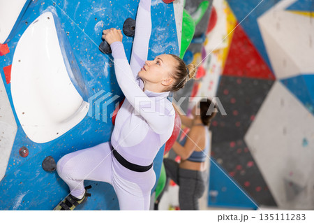 Concentrated woman moving up bouldering wall in climbing gym Concentrated woman moving up bouldering wall in climbing gym 135111283