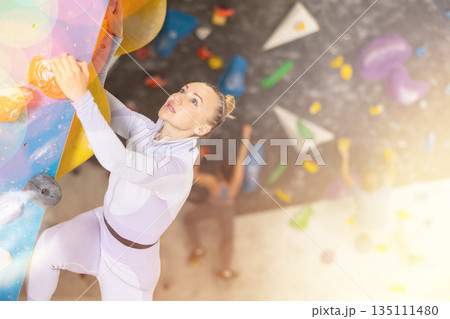 Adult woman practicing rock climbing on climbing wall Adult woman practicing rock climbing on climbing wall 135111480