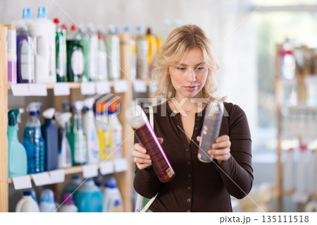 Happy young girl emotionally choosing aerosol hairspray in cosmetics store Happy young girl emotionally choosing aerosol hairspray in cosmetics store 135111518