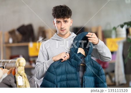 Young guy choosing down jacket in clothing store 135111520