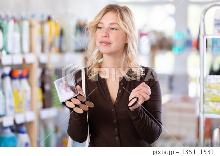 Girl housewife in cosmetic store examines goods, chooses eye shadow 135111531