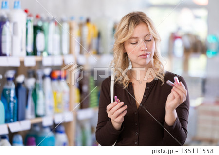 Girl housewife in cosmetic store examines goods, chooses facial powder Girl housewife in cosmetic store examines goods, chooses facial powder 135111558
