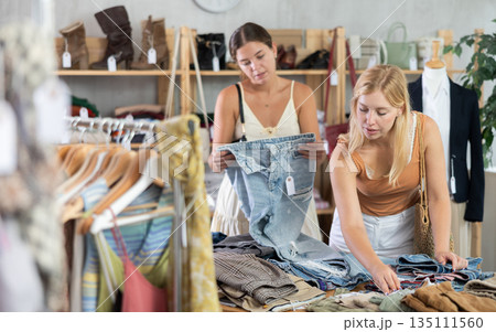 Fashionista girls near showcase examine goods, buying shorts or trousers Fashionista girls near showcase examine goods, buying shorts or trousers 135111560