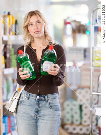 Focused young Woman choosing dishwashing liquid on supermarket shelf 135111652