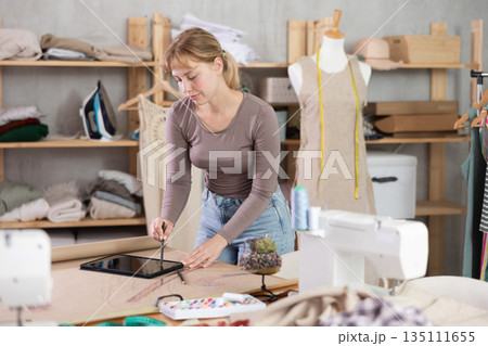 Female dressmaker working on digital sketch of dress in workshop 135111655