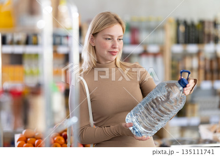 Girl buyers examine goods, choose large capacity bottle of water in store Girl buyers examine goods, choose large capacity bottle of water in store 135111741