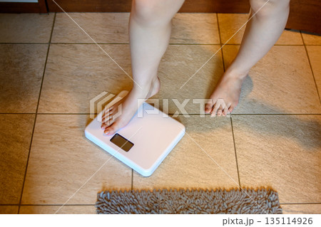 バスルームで体重を計る若い女性　洗面台の前で体重計に乗る足元　スレンダー　トリミングアップ 135114926