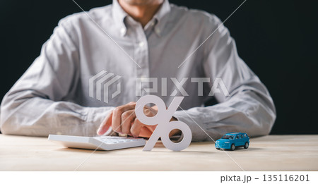 Person working on calculations for car interest rate, pressing buttons on calculator, miniature auto model rests near prominent percent sign representing finance loan options and sale 135116201