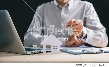 Real estate agent hand holds house key, desk features paper home model and property document, laptop screen shows mortgage loan for buying home, investors plan future ownership Real estate agent hand holds house key, desk features paper home model and property document, laptop screen shows mortgage loan for buying home, investors plan future ownership 135116215