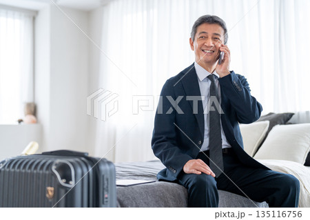 出張先からスマートフォンで通話をするシニア男性 出張先からスマートフォンで通話をするシニア男性 135116756