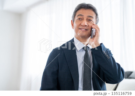 出張先からスマートフォンで通話をするシニア男性 出張先からスマートフォンで通話をするシニア男性 135116759