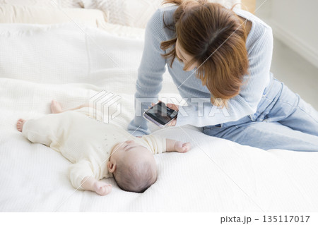 赤ちゃんをスマホで撮る若い母親 135117017