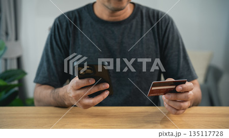 Man hands holding credit card and using smartphone for online shopping at home. Concept of mobile banking, e-commerce, digital payment, secure transaction, and financial technology. 135117728