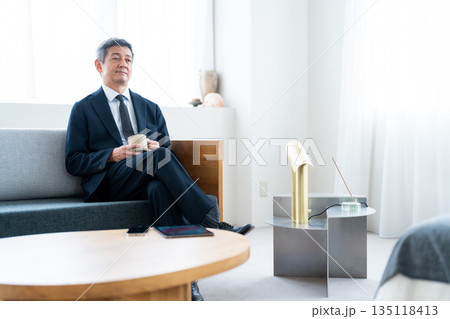 ホテルのソファでコーヒーを飲みながら寛ぐビジネスマン 135118413