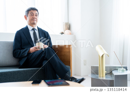ホテルのソファでコーヒーを飲みながら寛ぐビジネスマン ホテルのソファでコーヒーを飲みながら寛ぐビジネスマン 135118414