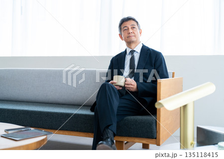 ホテルのソファでコーヒーを飲みながら寛ぐビジネスマン 135118415