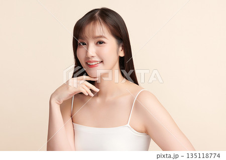 A beautiful young Asian woman with clean, fresh skin against a beige background. Skincare, facial treatment, cosmetology, beauty, and spa. An elegant portrait of an Asian woman. 135118774