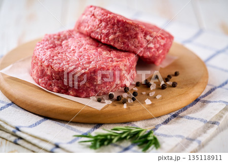 Two raw beef burger patties with peppers and salt on a white table. Ideal ingredient for grill, BBQ . 135118911