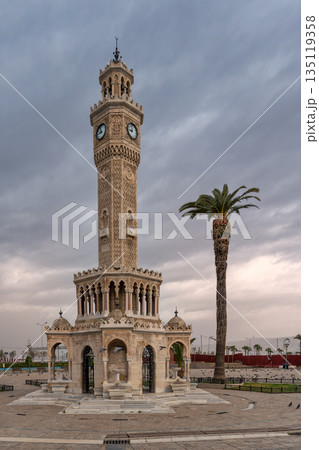 Iconic Konak Clock Tower and a tall palm tree in Konak Square, Izmir, Turkey, under a cloudy sky. 135119358
