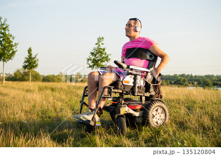 Disabled man sitting in a wheelchair listening to music while spending time in nature. 135120804