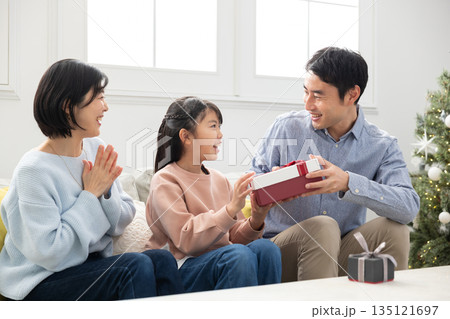 両親からクリスマスプレゼントをもらって喜ぶ小学生の女の子 両親からクリスマスプレゼントをもらって喜ぶ小学生の女の子 135121697