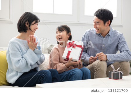両親からクリスマスプレゼントをもらって喜ぶ小学生の女の子 135121700