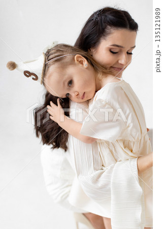A mother tenderly embraces her young daughter, creating a heartwarming scene of love and affection. 135121989