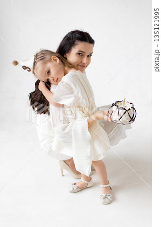 A mother and daughter celebrate a birthday together, with a cake and party hat. 135121995