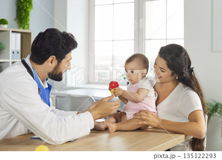 Pediatrician interacting with a happy baby and mother in a bright clinic office 135122293