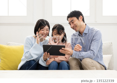 タブレットでビデオ通話する笑顔の3人家族 タブレットでビデオ通話する笑顔の3人家族 135122339