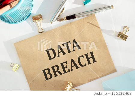 DATA BREACH text printed on craft envelope lying on white background next to office tools 135122468