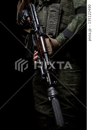 Closeup photo of man's hand holding machine gun. Man is wearing military uniform. 135122490