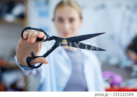 Artistic young woman demonstrating mastery with large tailoring scissors in creative studio setting 135122509
