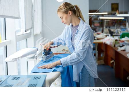 Craftswoman skillfully presses fabric, clothing artisan expertly ironing fabric 135122515